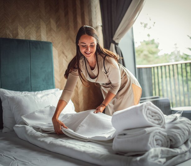 Mitarbeiterin des Housekeepings bereitet das Bett im Hotelzimmer auf | © Getty Images